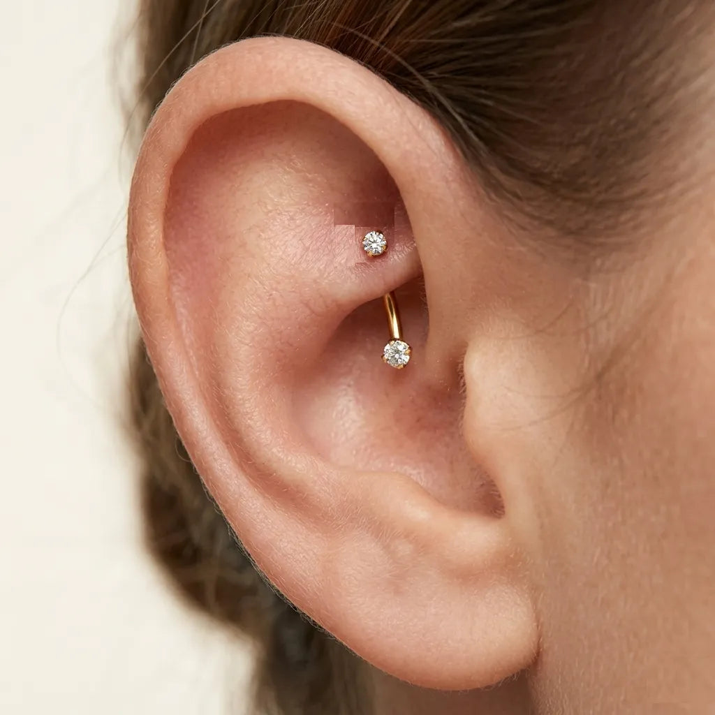 Close-up of an ear with a gold earring featuring a clear gemstone on a neutral background