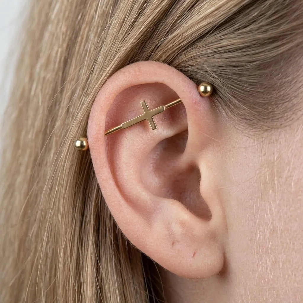 Gold cross-shaped earring worn on a person's ear