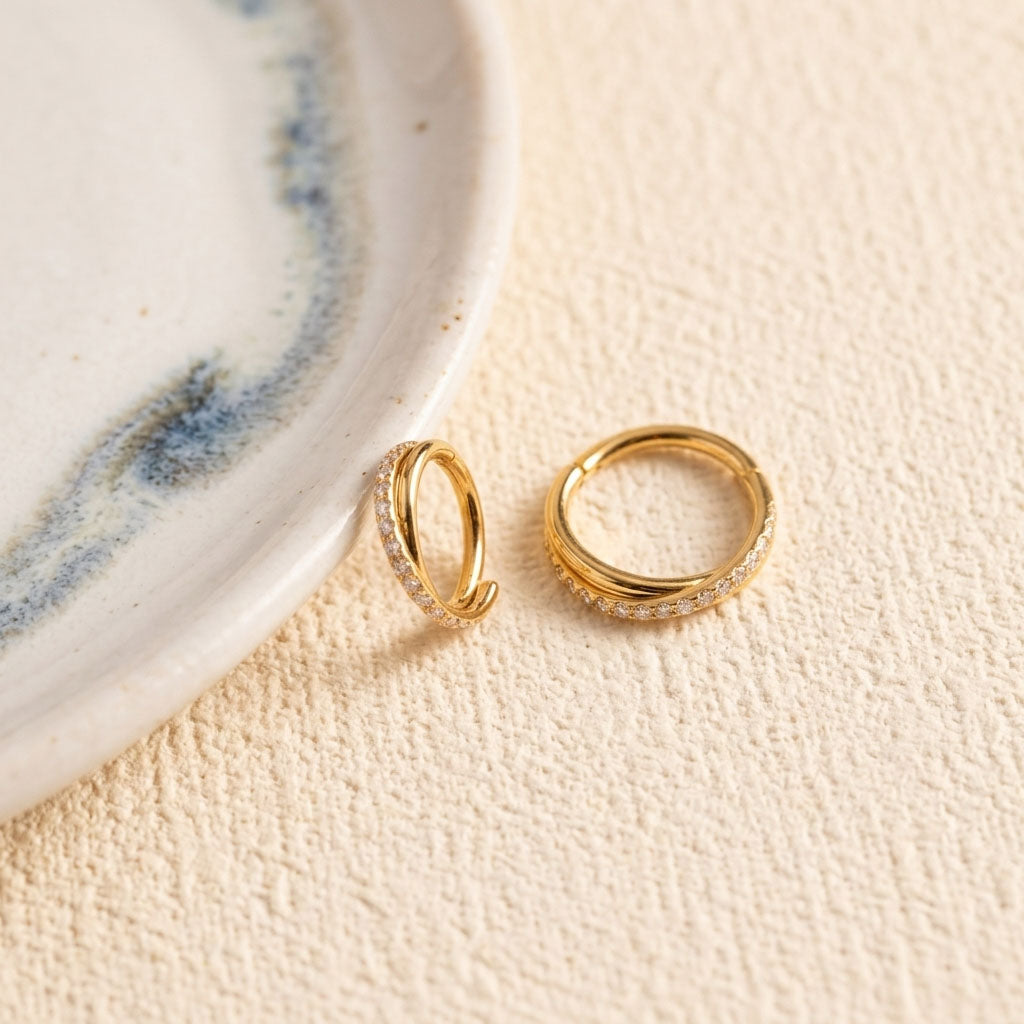 Two gold rings with gemstones on a textured beige surface.