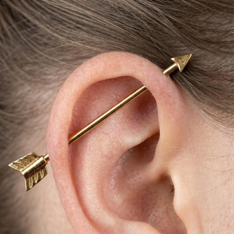 Gold arrow-shaped earrings worn on an ear with a blurred background
