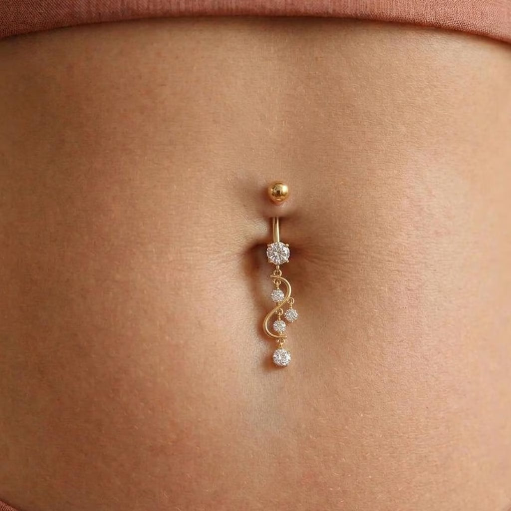 A close-up of a gold belly button ring with clear rhinestone accents, worn on a person's navel.