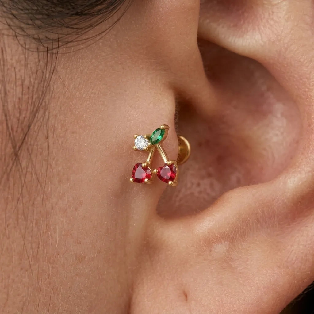 Close-up of an ear wearing a gold earring with red and green gemstones.
