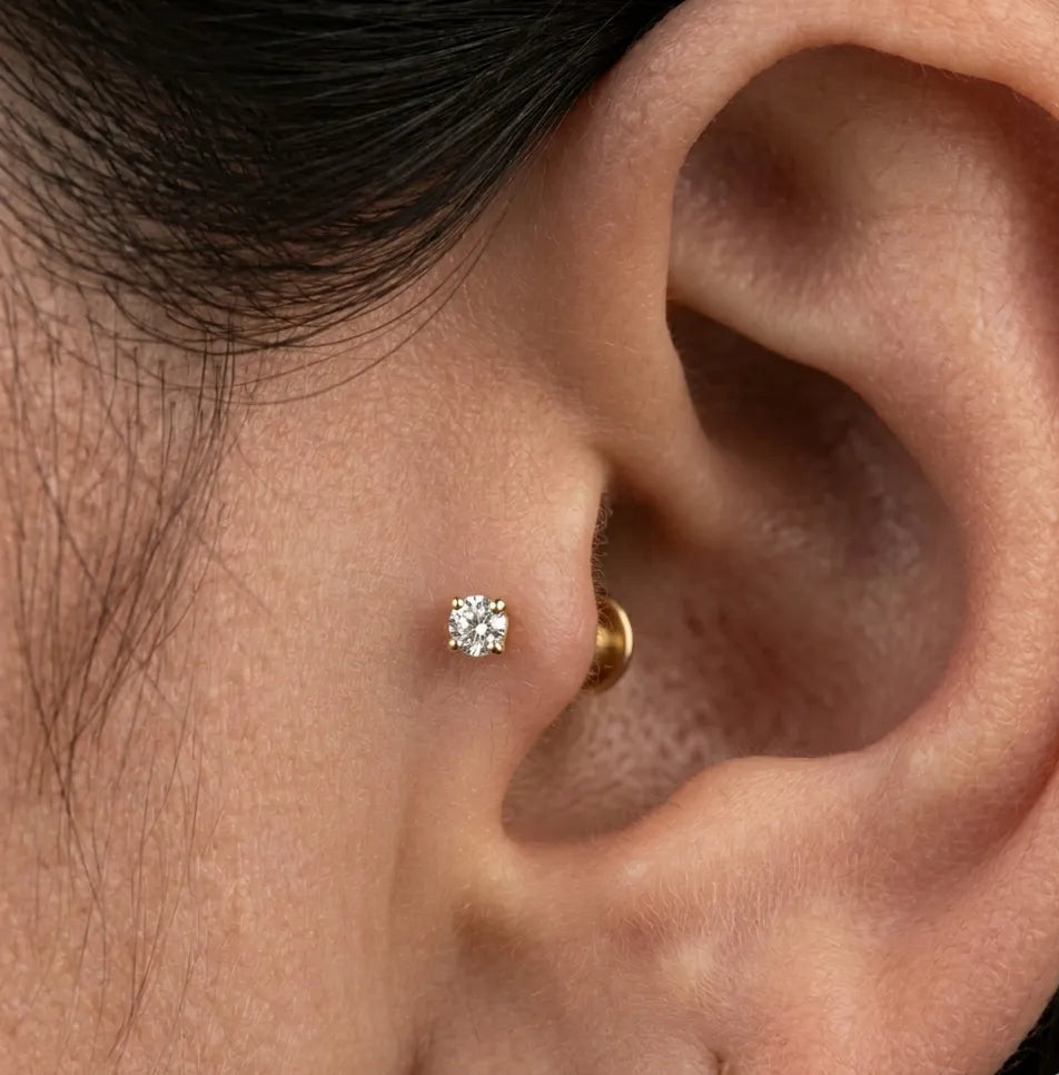 Close-up of an ear wearing a gold stud earring with a clear gemstone.