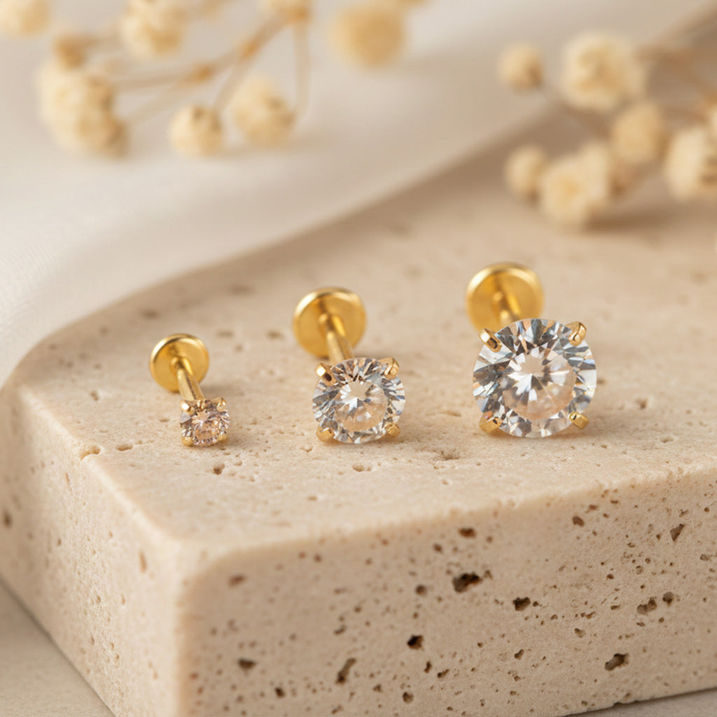 Gold stud earrings with clear gemstones on a beige stone surface