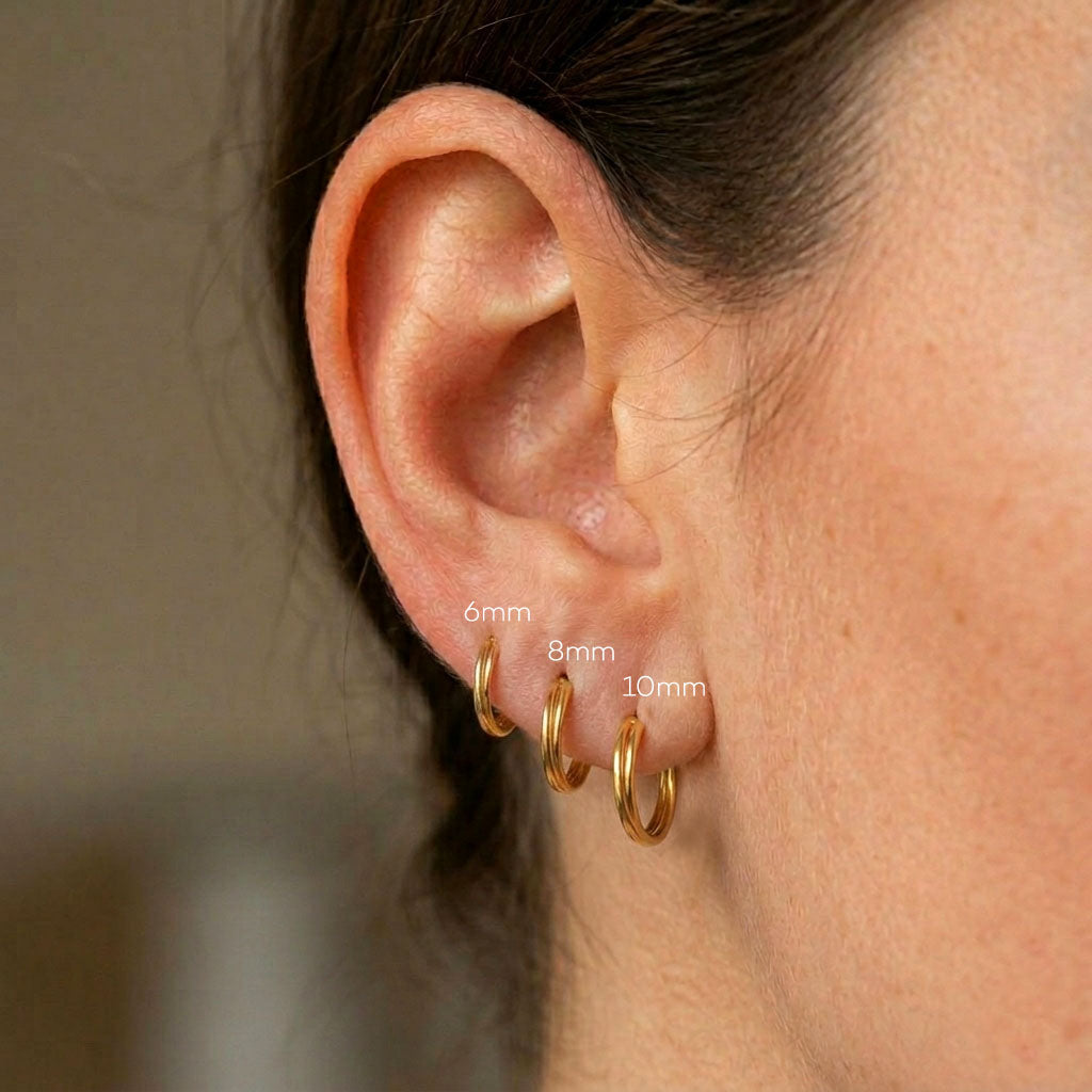Close-up of an ear wearing gold hoop earrings with size labels.