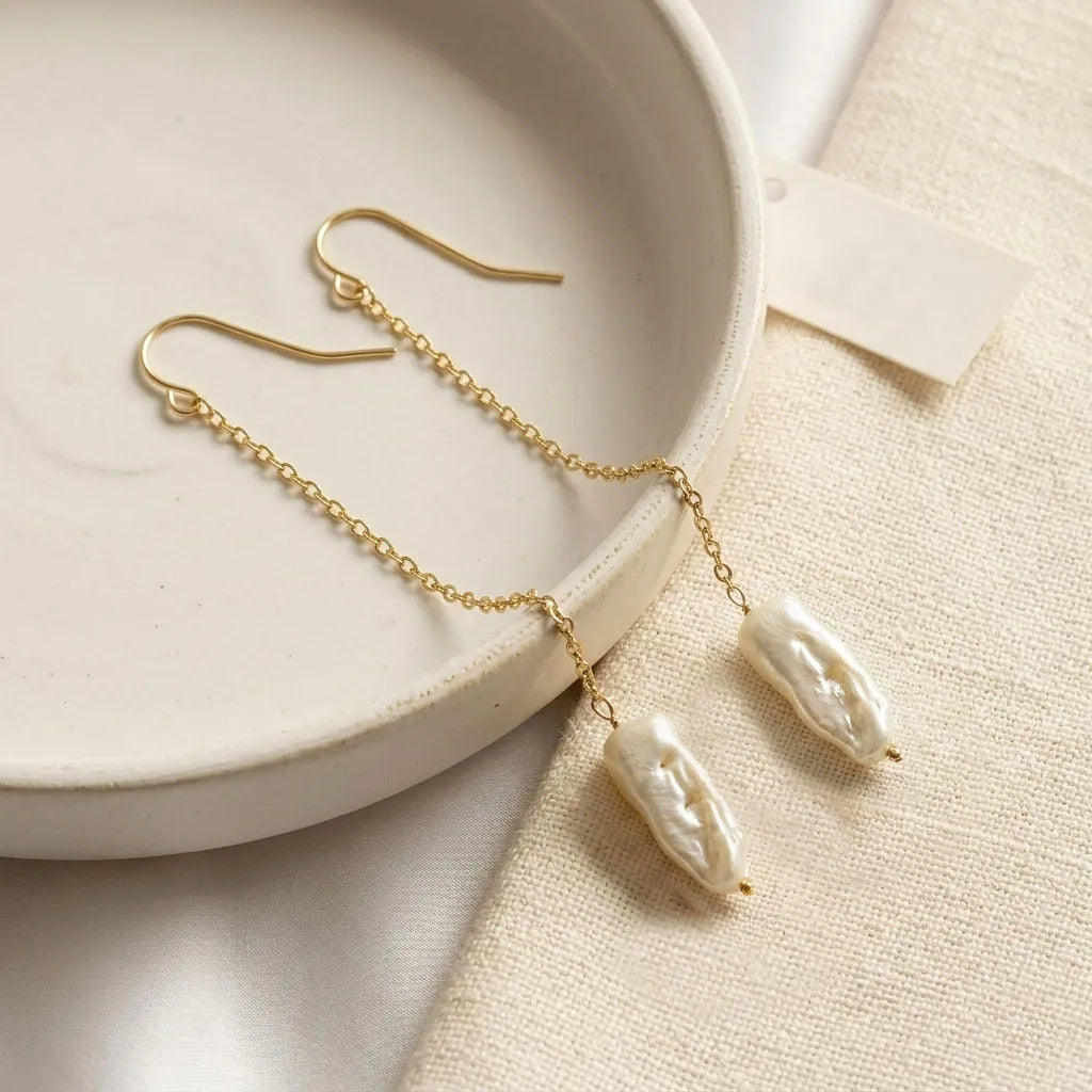Gold earrings with pearl-like beads on a beige plate