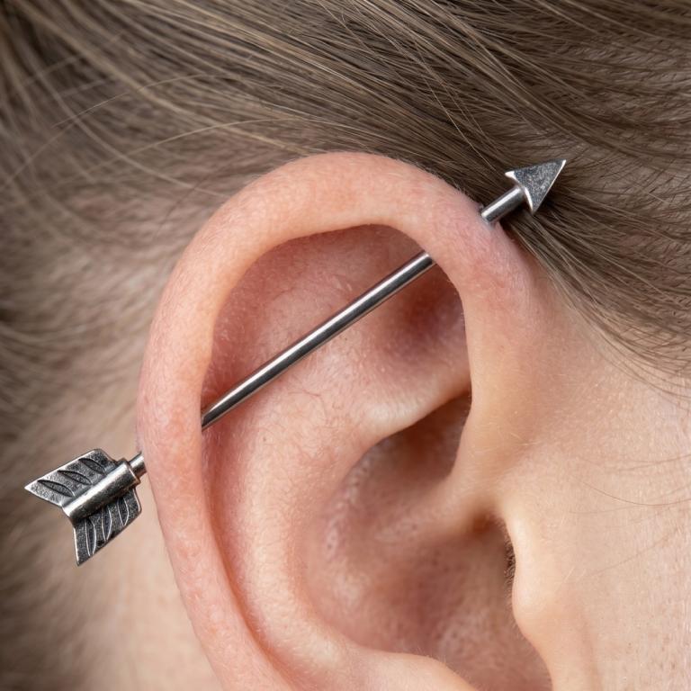 Close-up of an ear with two silver arrow-shaped earrings.