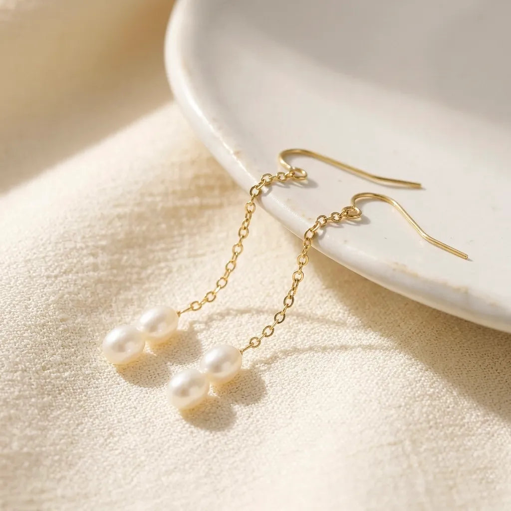 Gold earrings with pearl drops on a beige surface