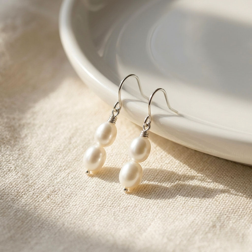 Pearl earrings on a beige surface with a white plate in the background
