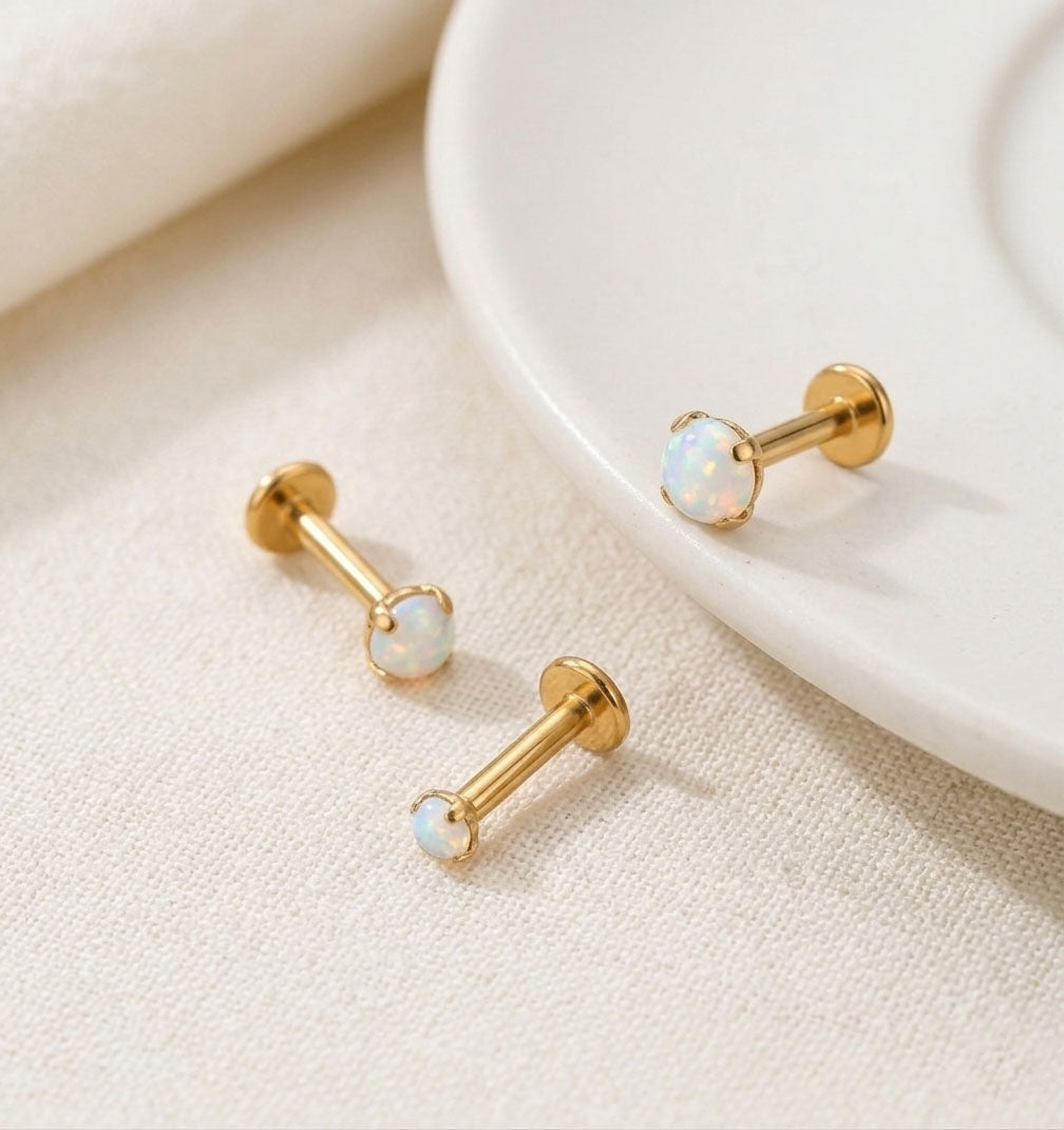 Gold barbell earrings with opal beads on a beige surface