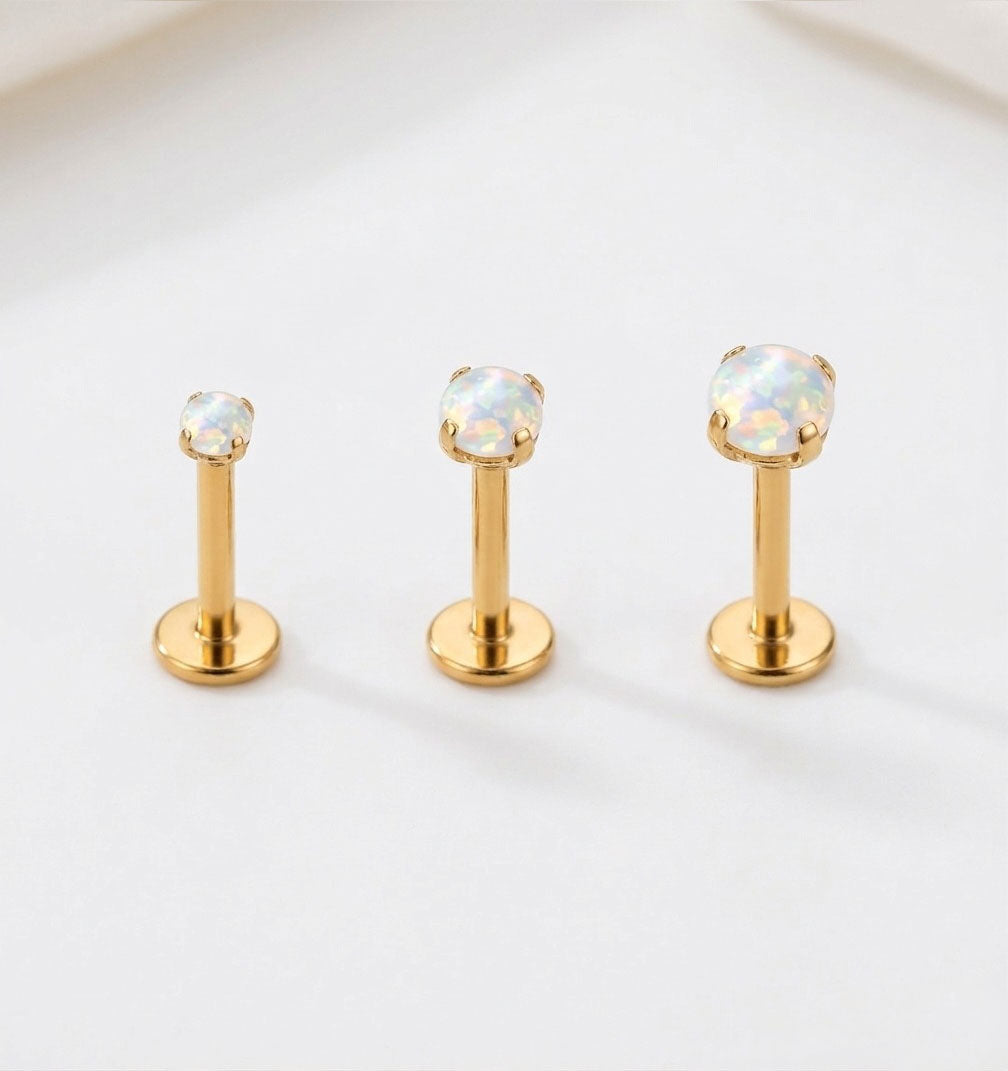 Three gold lip rings with opal stones on a light gray background