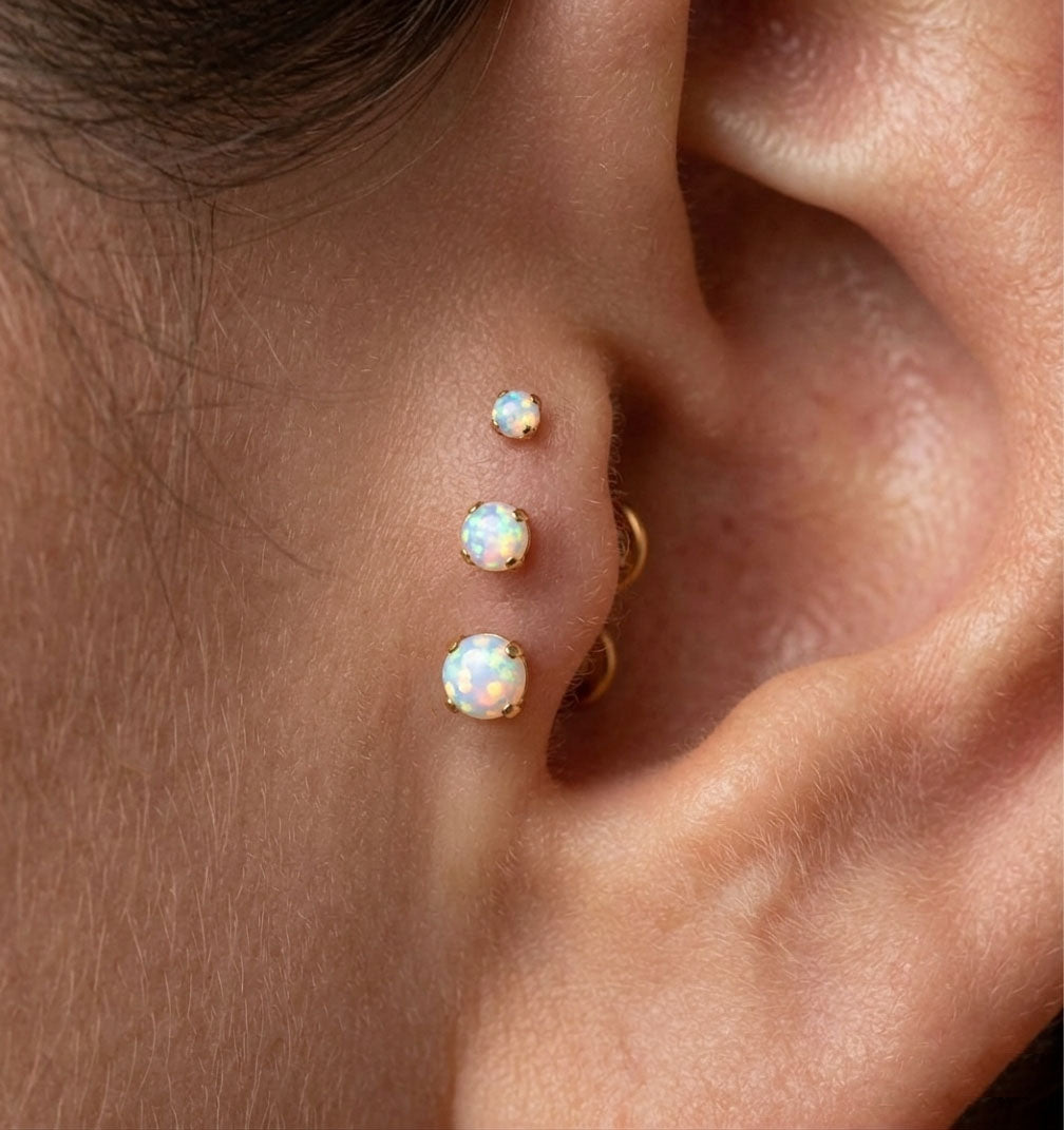 Close-up of an ear with opal earrings on a neutral background