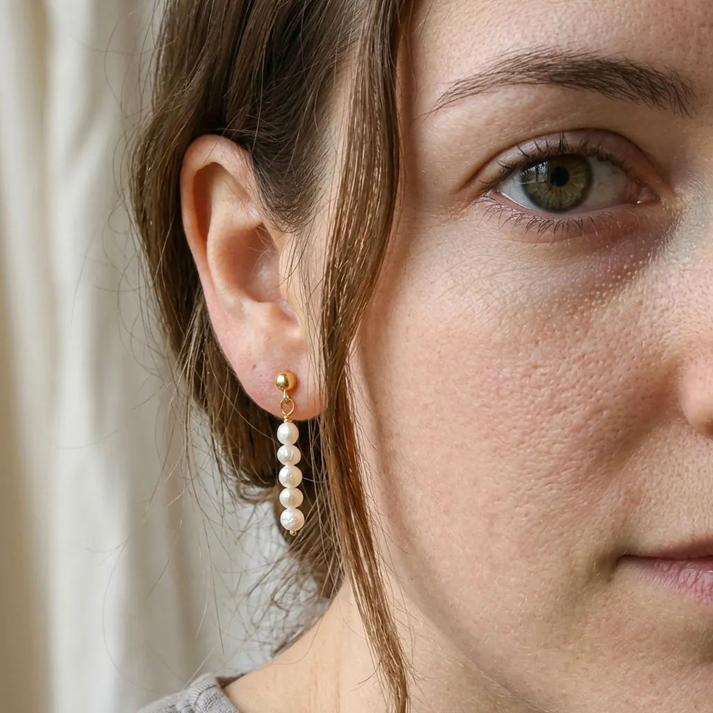 Model wearing Lys Doré gold baroque pearl drop earrings, face-on portrait