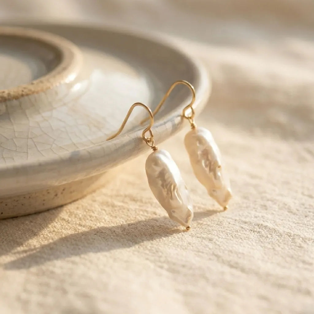 A pair of Perla Opaline earrings with organic pearls on gold filled hooks, displayed on a minimalist background.