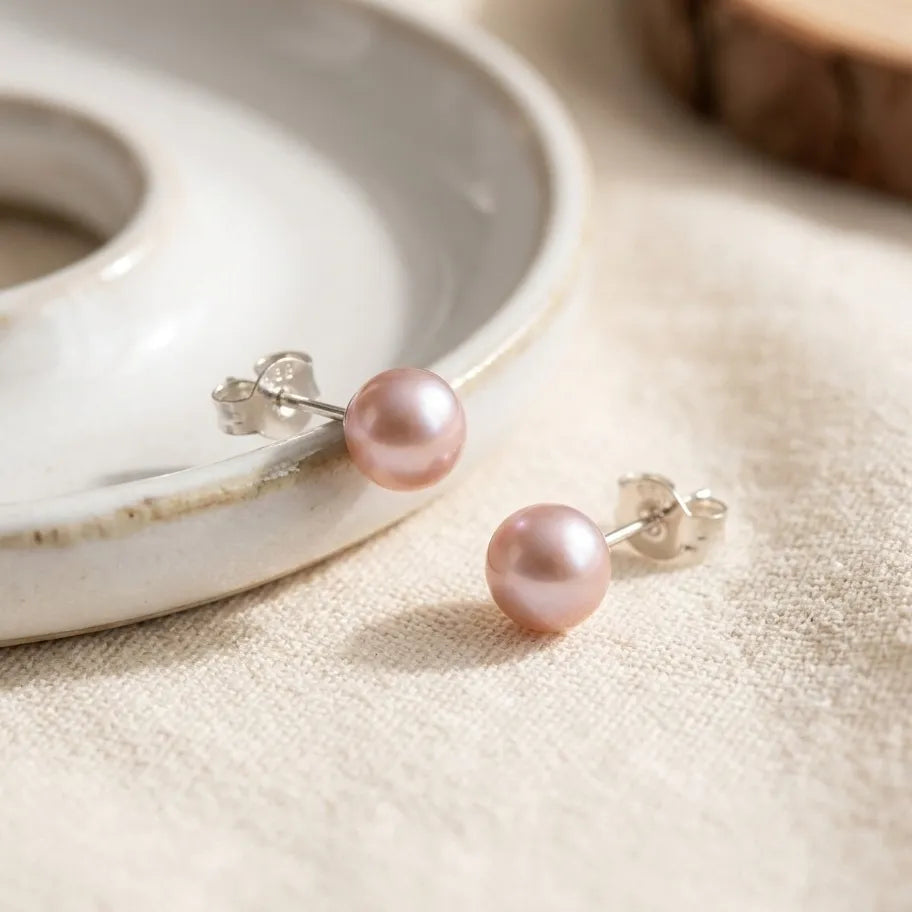 Pink pearl earrings on a textured surface with a ceramic dish in the background