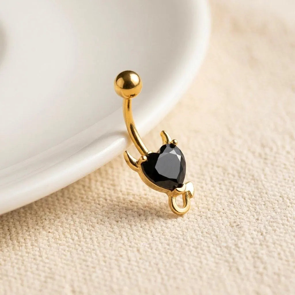 Gold belly button ring with a black gemstone on a beige surface