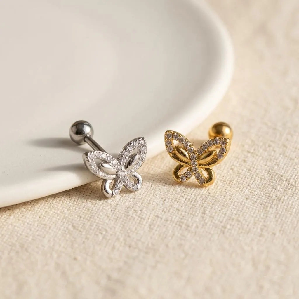 Butterfly-shaped earrings in gold and silver on a beige surface with a white dish.