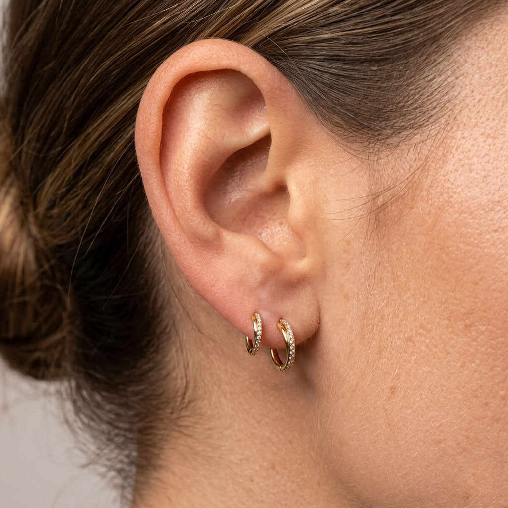 Close-up of an ear wearing gold hoop earrings with a neutral background