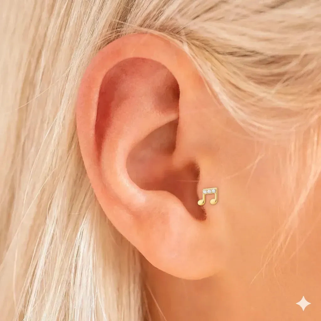 Gold music note earring on a person's ear with blonde hair.
