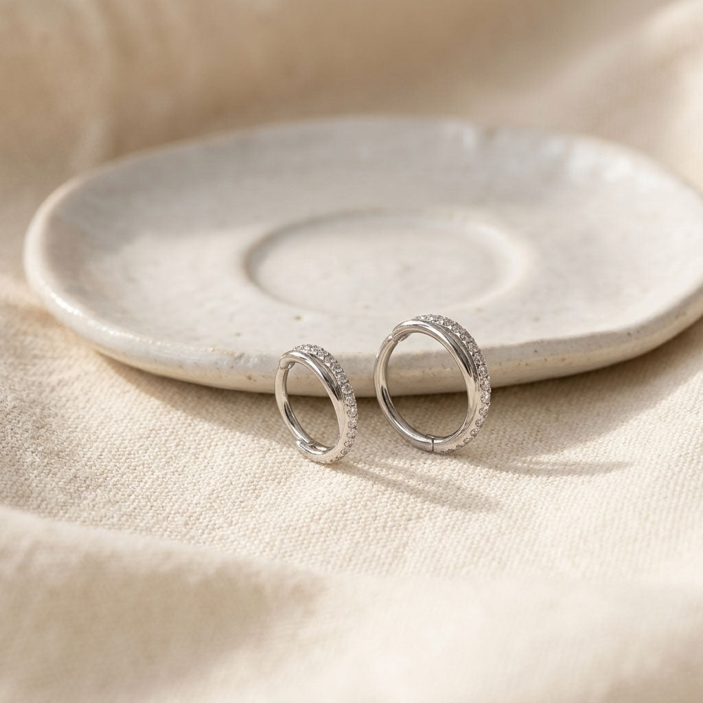 Silver hoop earrings on a white ceramic plate with a beige fabric background