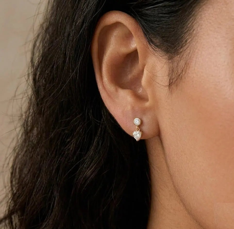 Close-up of an ear wearing a diamond earring with dark hair and beige background