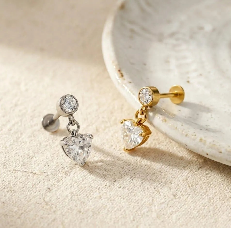 Gold and silver earrings with heart-shaped gemstones on a beige surface.