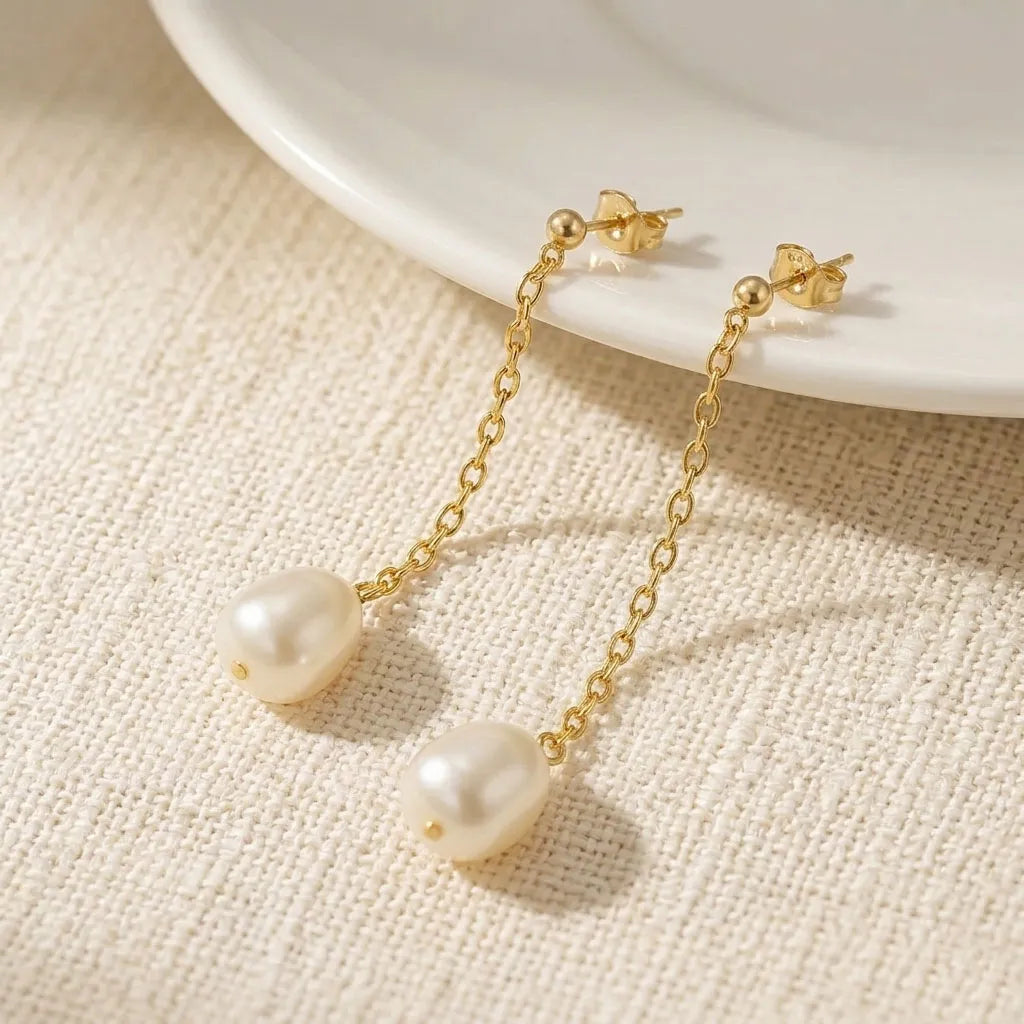 Pearl earrings with gold chains on a textured surface