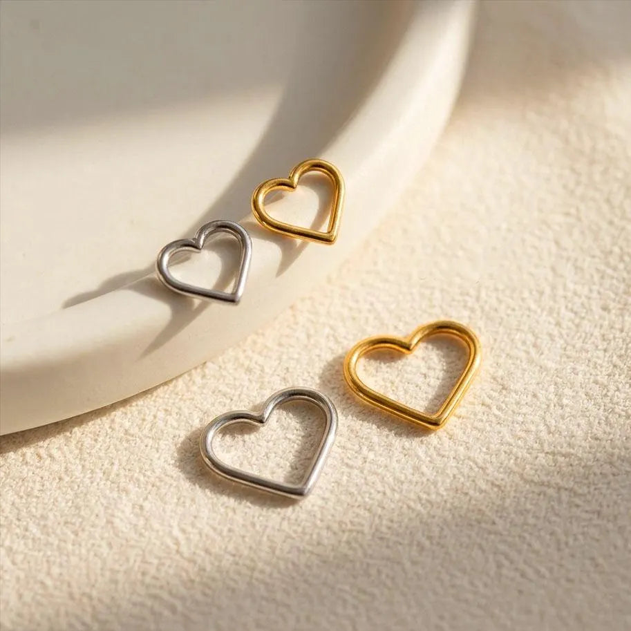 Three heart-shaped earrings in gold and silver on a textured beige surface.