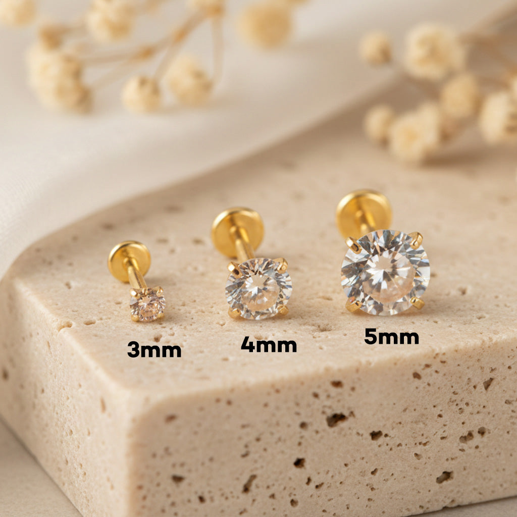 Gold stud earrings with varying sizes displayed on a beige surface.
