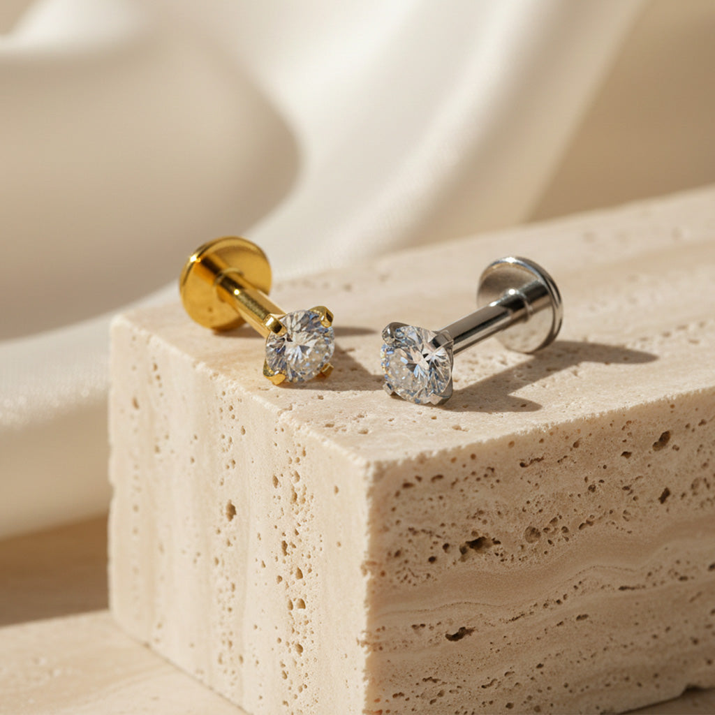 Two gold and silver stud earrings on a beige stone surface