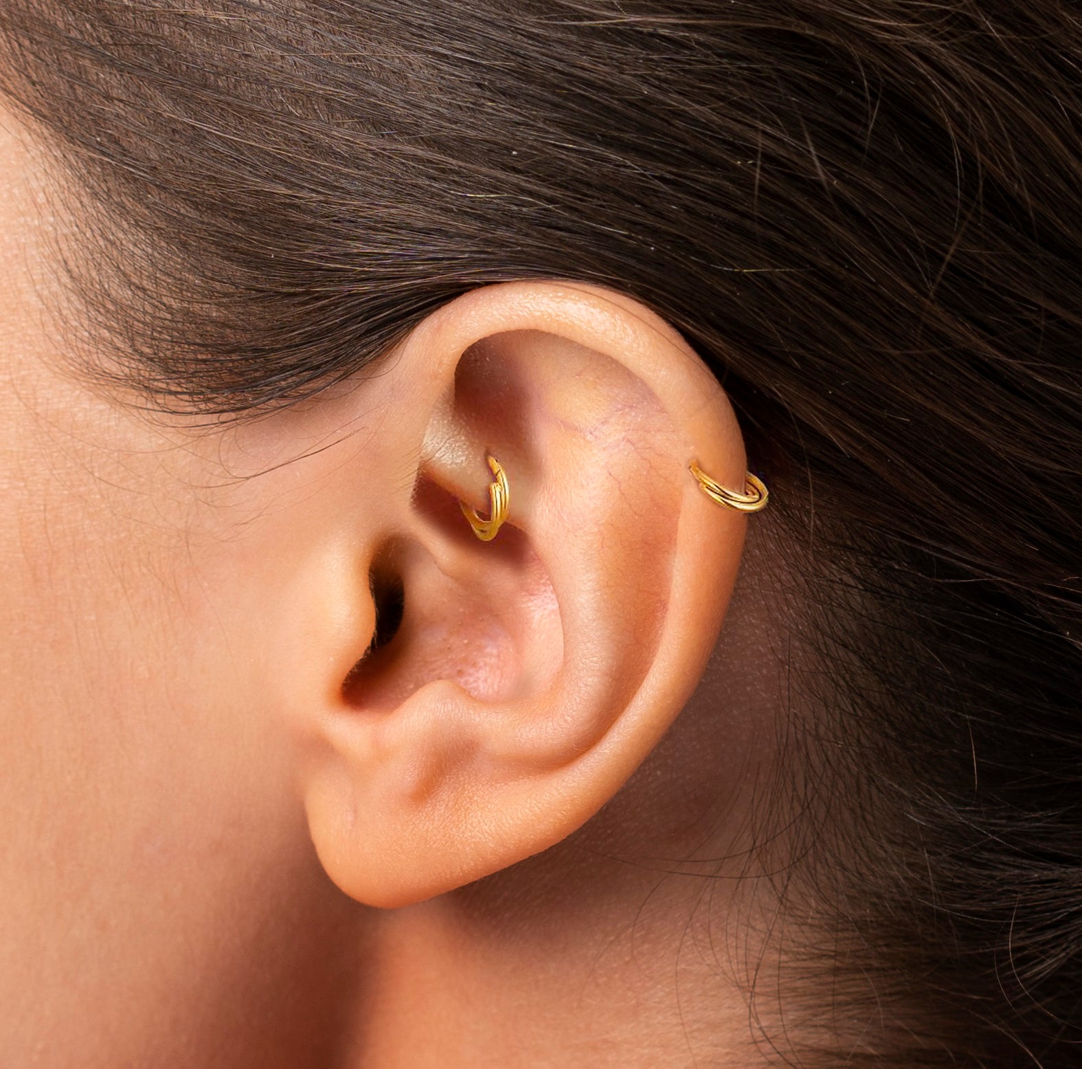 A close-up image of a person's ear wearing a gold-colored rook piercing.