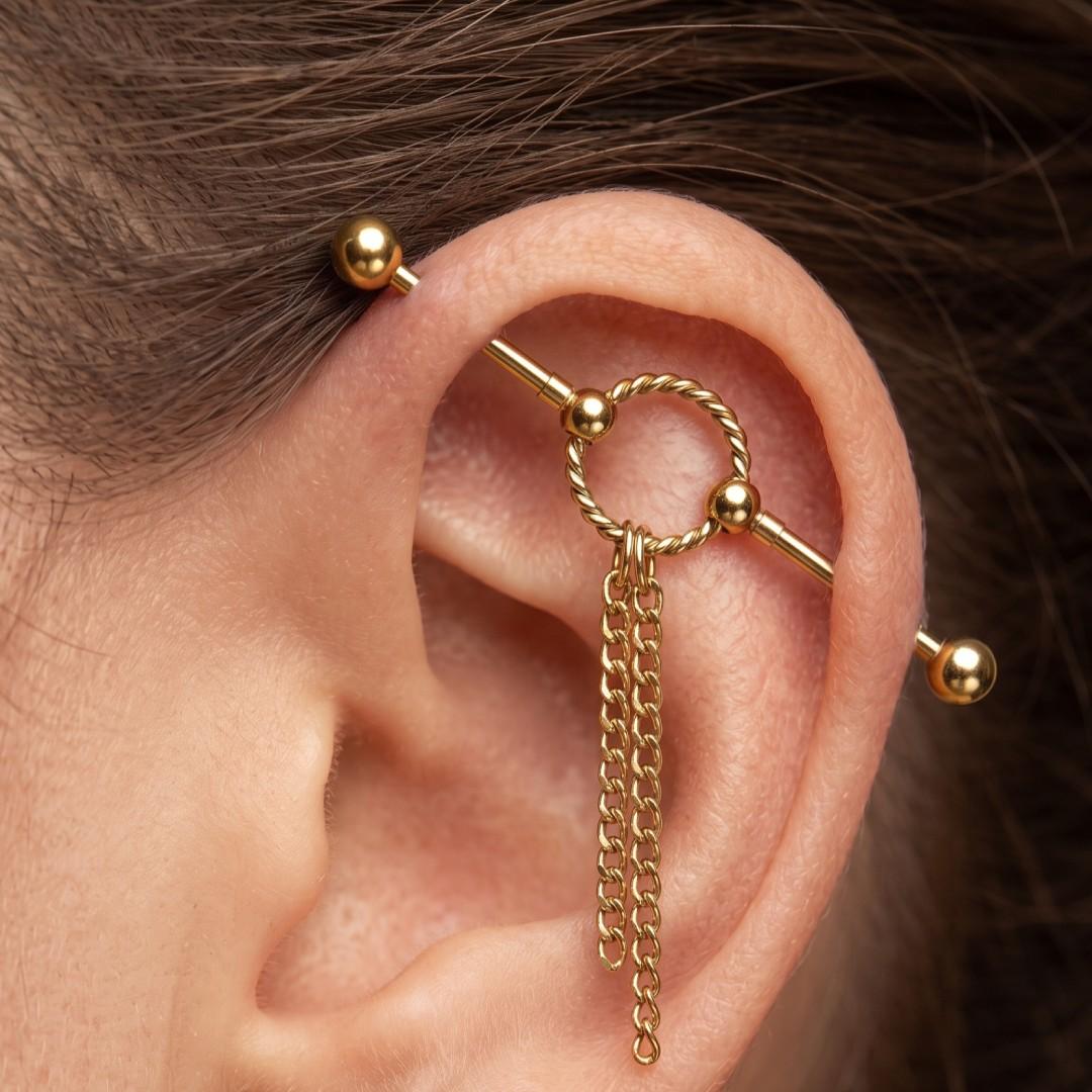 Gold ear cuff jewelry with a twisted hoop, small beads, and a dangling chain, shown worn on a person's ear with additional ear piercings visible.