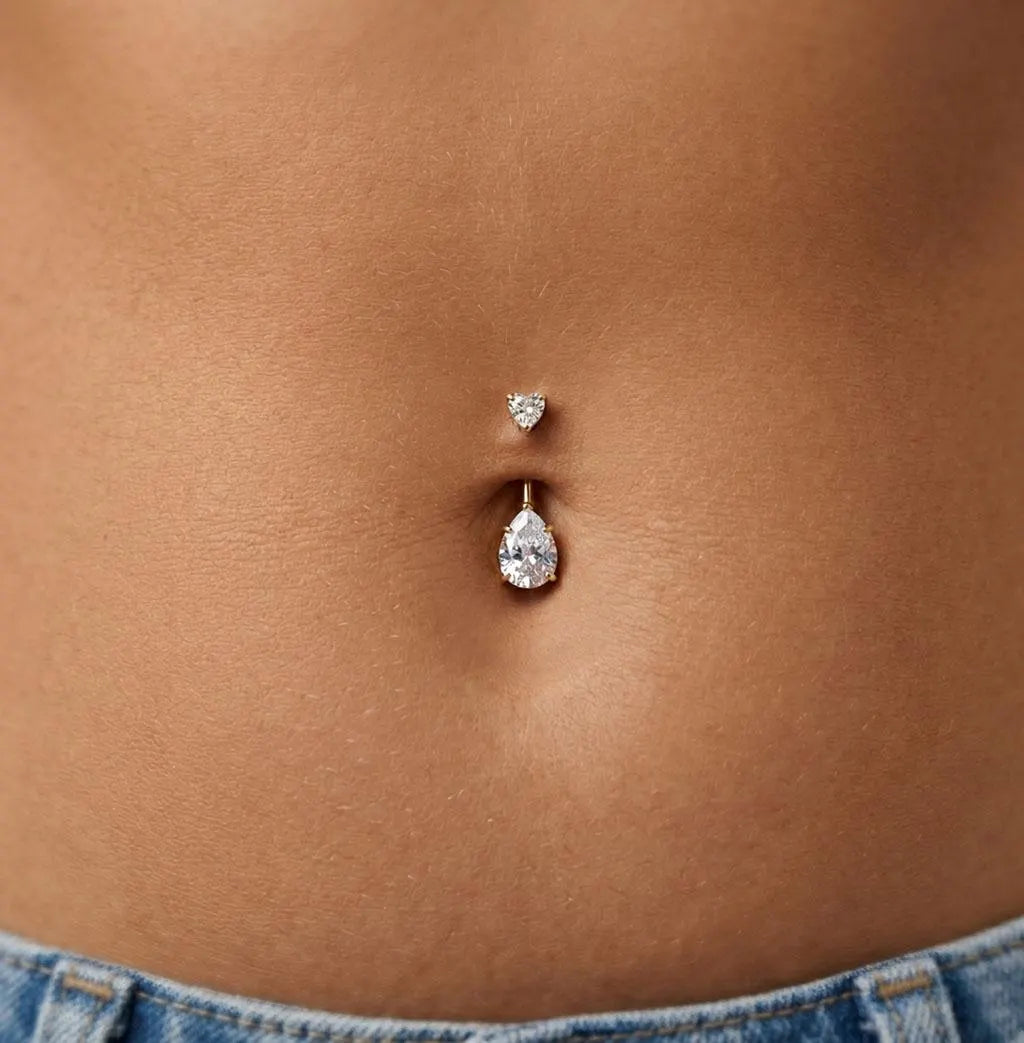 Close-up of a belly button with two silver belly buttons on a person wearing jeans.