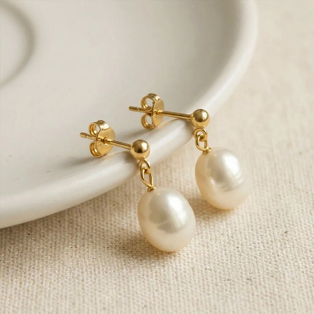 Pearl stud earrings with gold posts on a beige fabric background