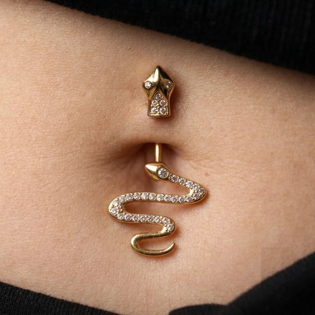 Gold snake-shaped belly button ring with clear rhinestones, shown worn on a person's navel.