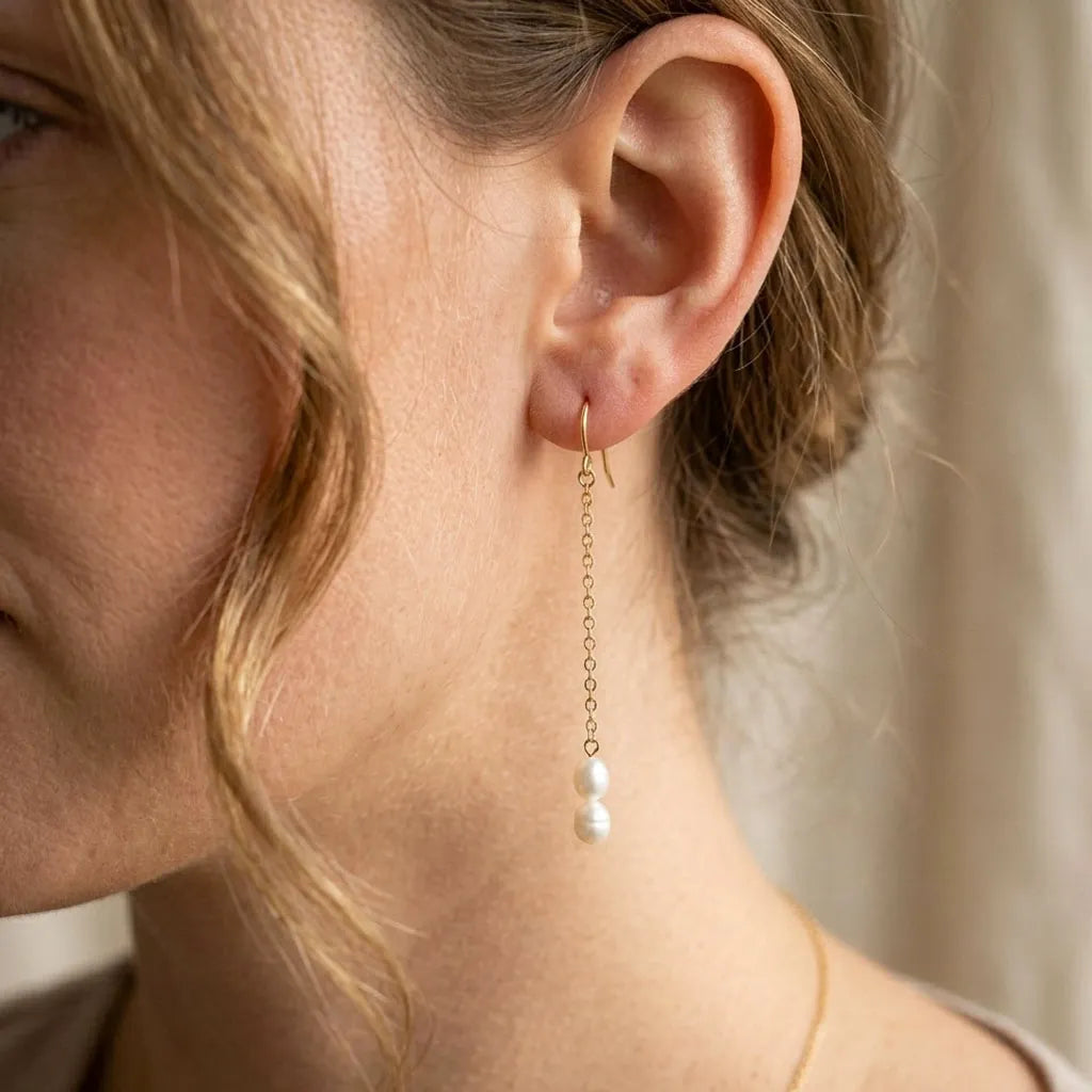 Close-up of a person wearing a gold earring with a pearl drop.