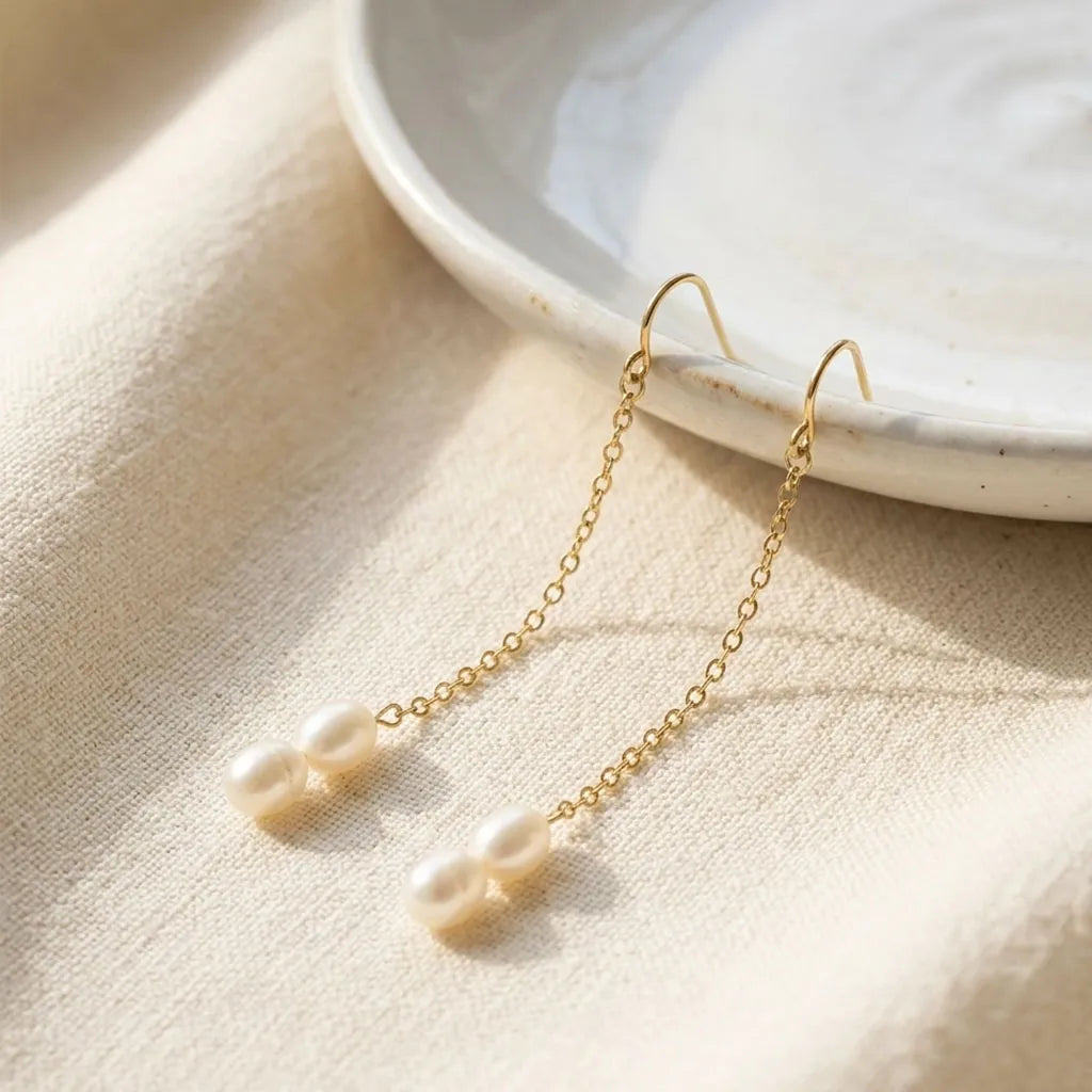 Gold earrings with pearl drops on a beige surface