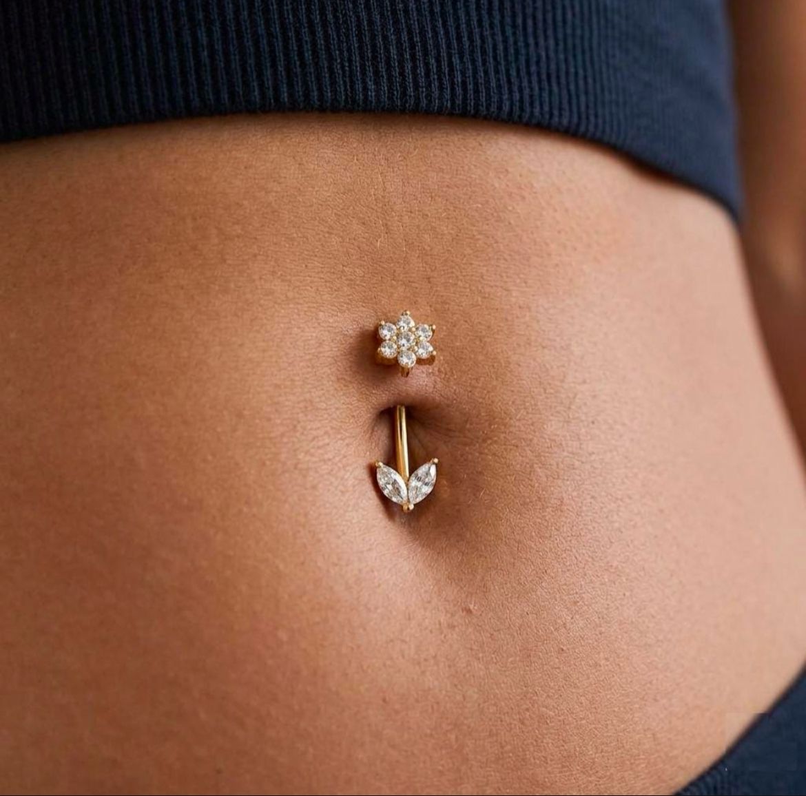 Gold belly button ring with floral design on a person's belly button.