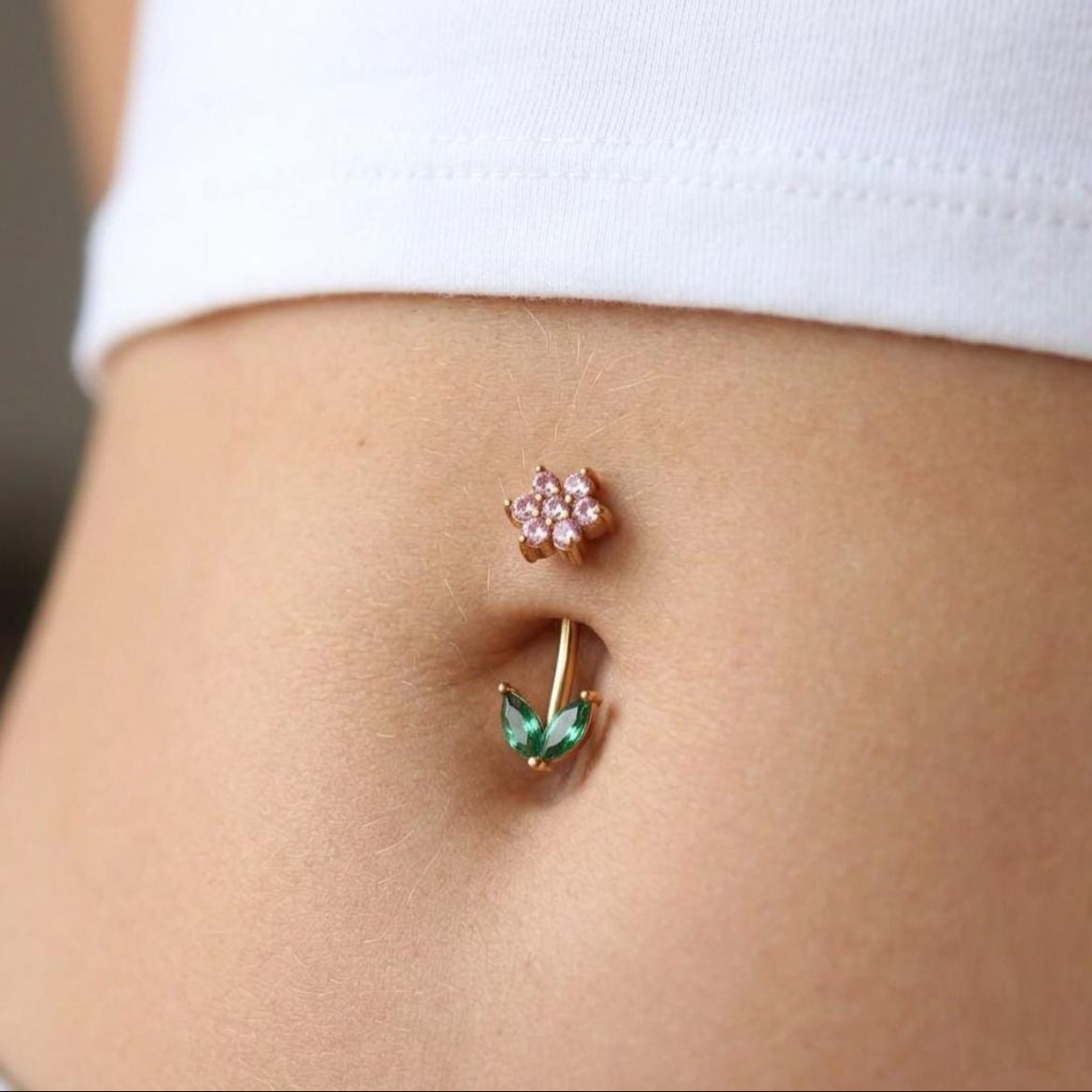 Close-up of a person's belly button with floral-shaped belly button rings.
