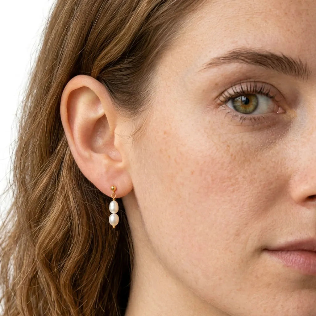 Close-up of Fleur Celeste gold pearl drop stud earrings on model's ear