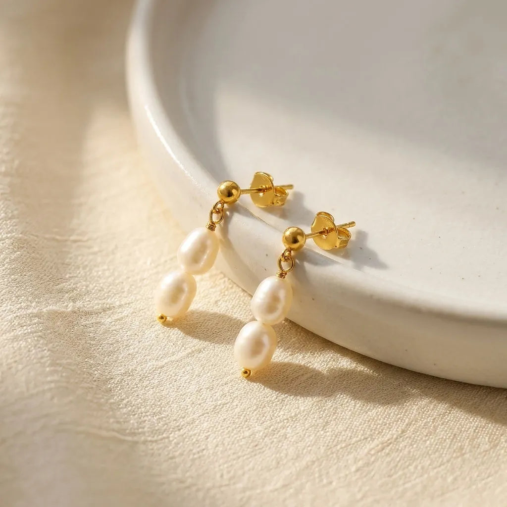 Fleur Celeste gold stud earrings with graduated freshwater pearl drop on white ceramic dish