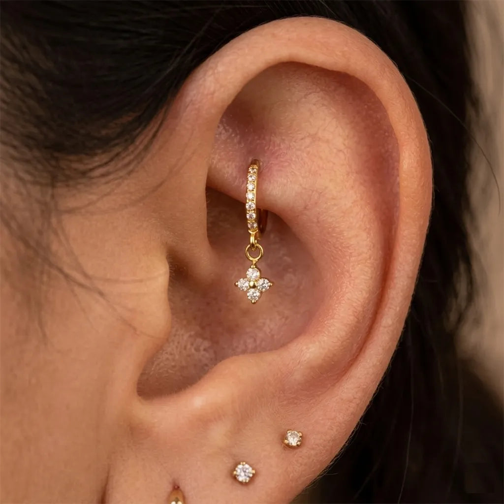 Gold four-petal CZ flower charm pavé hoop worn in rook piercing