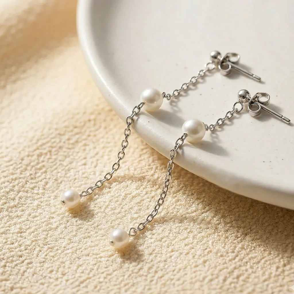 Symmetrical front view of sterling silver long chain pearl drop earrings worn by a model