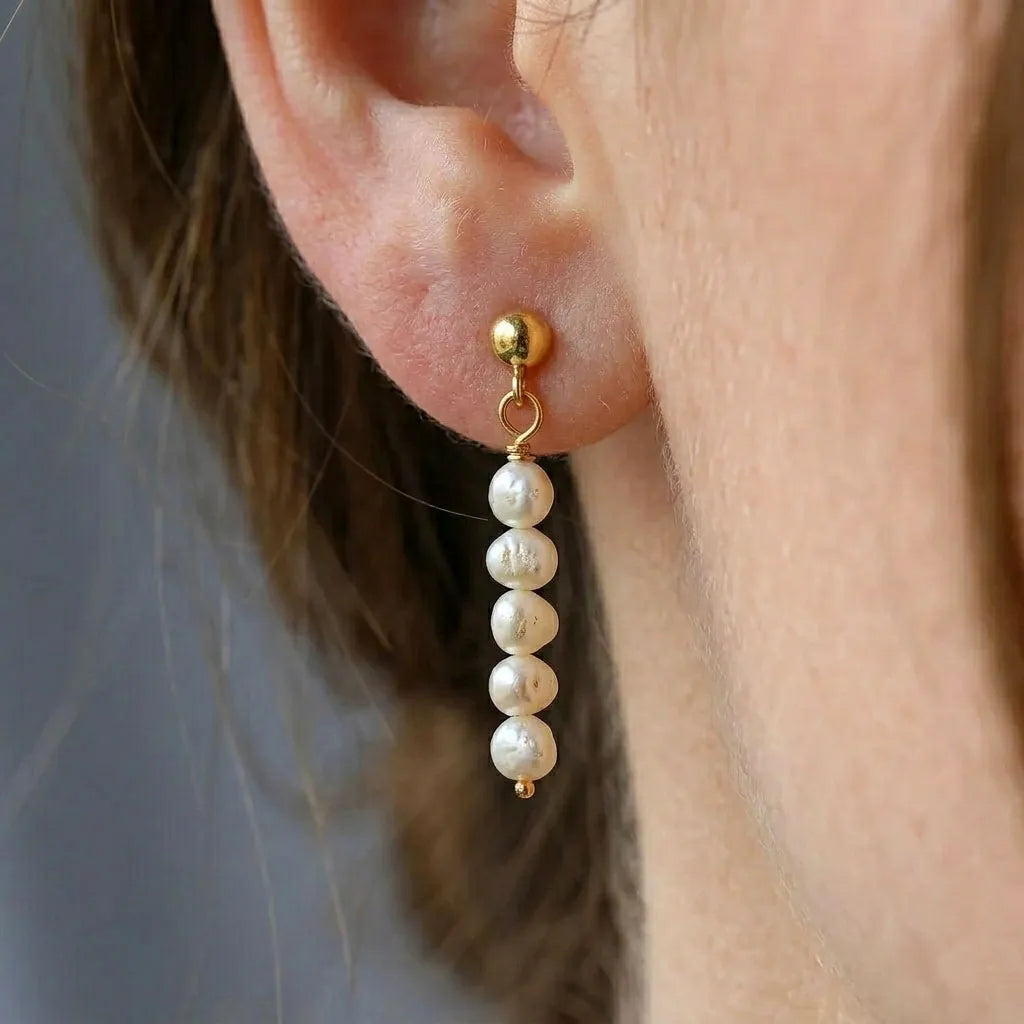 Close-up of Lys Doré gold baroque pearl stud drop earrings worn on model's ear