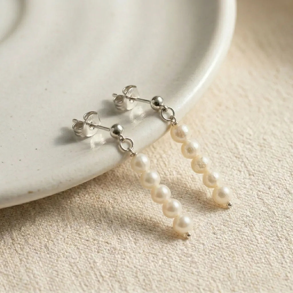 Lys Doré sterling silver stud earrings with freshwater pearl drop on white ceramic dish