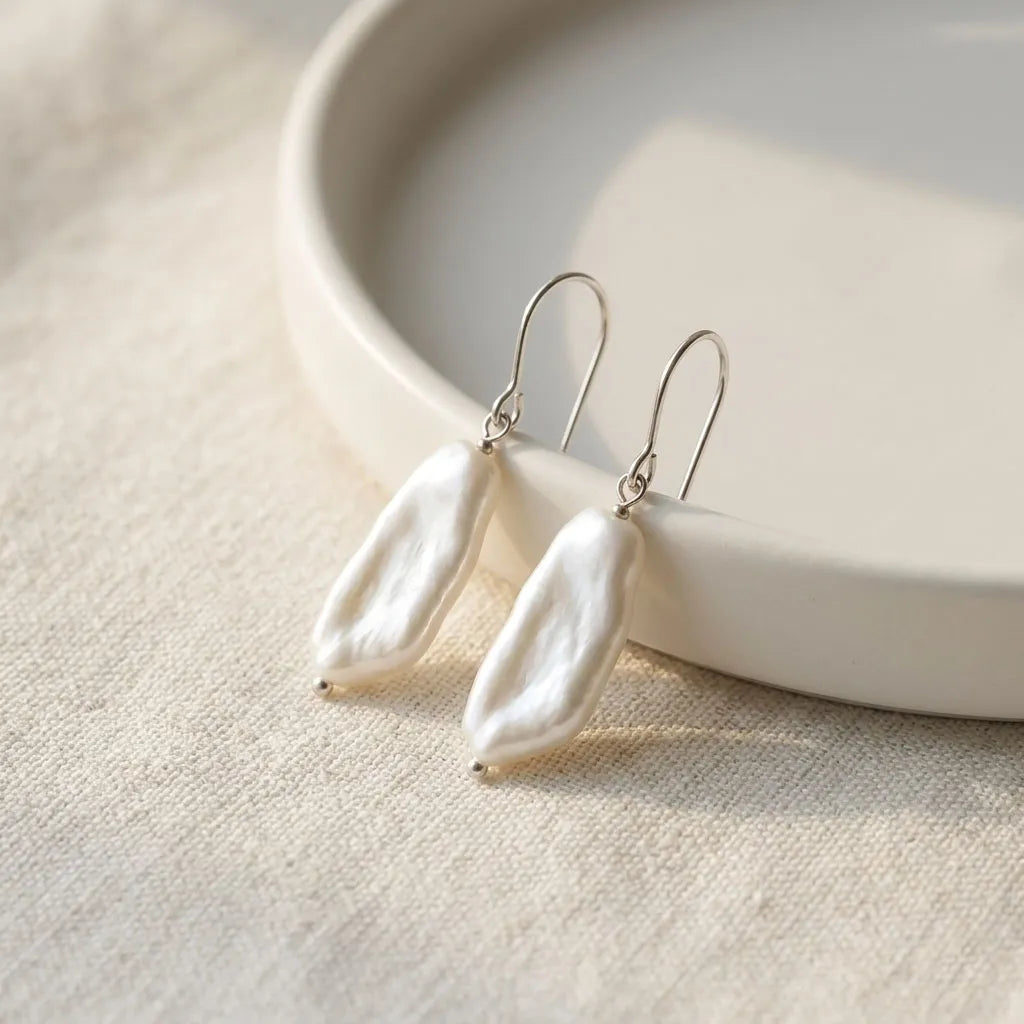A pair of natural white baroque pearl earrings with silver French hooks, elegantly resting on the linen background.