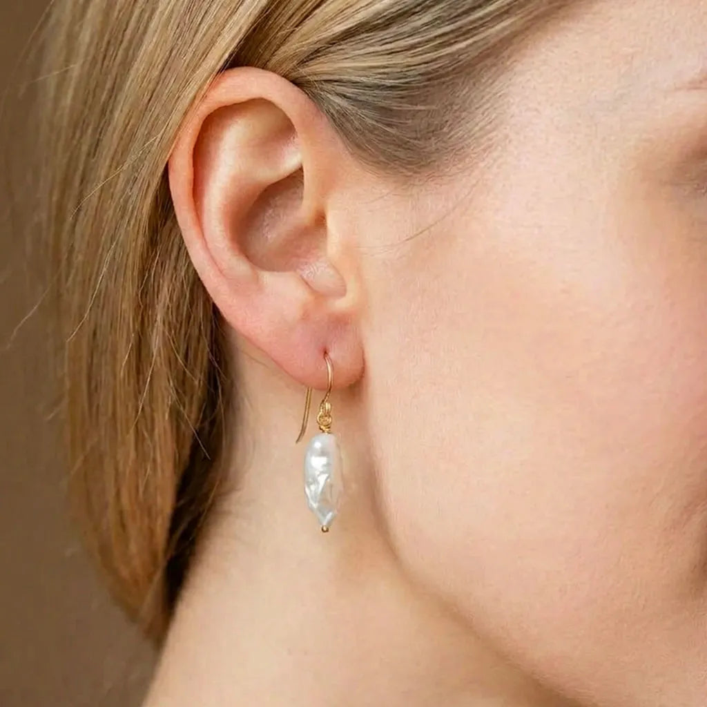 Close-up view of the Perla Opaline pearl drop earrings being worn, showing how the gold hooks sit elegantly on the ear