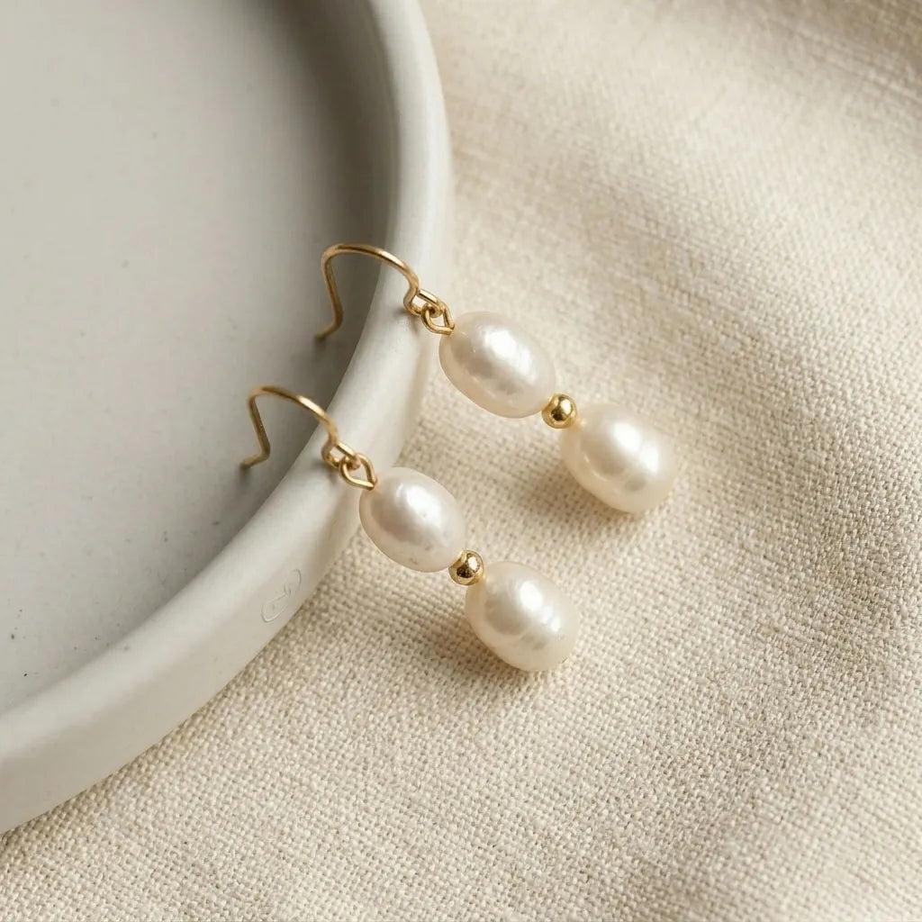 Close-up of Solea Alba double pearl hook earrings showing gold bead detail and oval freshwater pearls