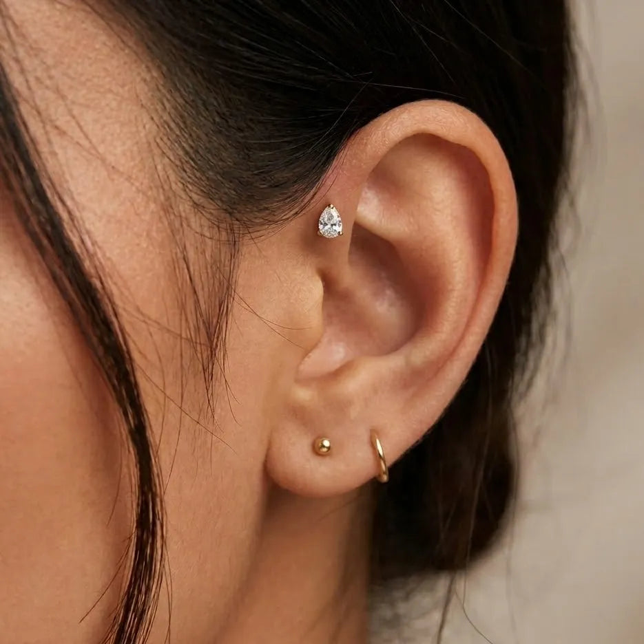 Close-up of ear wearing gold titanium teardrop gem tragus piercing